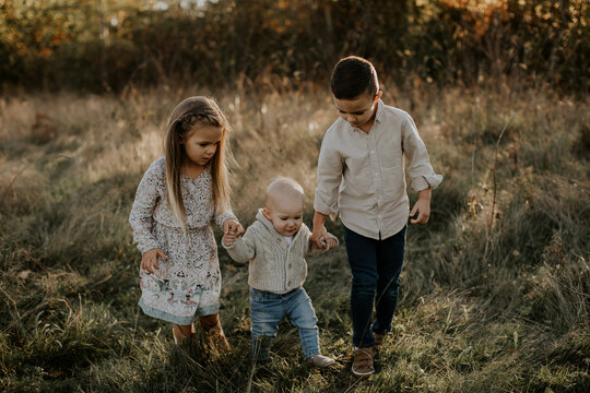 Older siblings assist their younger baby brother with walking