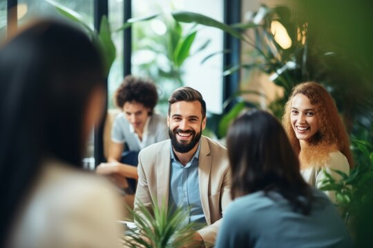 Young happy businessman leading a briefing meeting with his diverse team in a green modern office