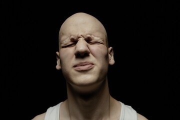 Portrait of pale bald man with screwed up eyes experiencing sudden panic attack captured against black background in studio with low key light, mental, health, disorder concept, copy space