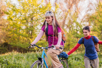 Obraz premium Happy lesbian couple pushing bicycle in nature enjoying vacation together
