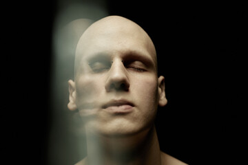 Close up portrait of bald pale man with bridge piercing addressing his inner thoughts while standing in top side light against black background in low key lit studio, lens flare effect, copy space