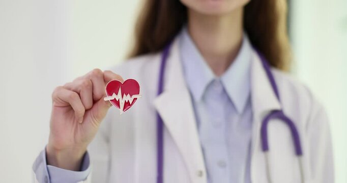 Woman doctor shows tiny heart brooch in private clinic. Cardiologist with stethoscope holds accessory reminding about health in hospital