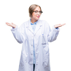 Beautiful young blonde doctor woman wearing white coat over isolated background clueless and...