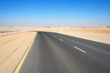 Winding black asphalt road through the sand dunes of  United Arab Emirates. An asphalt road zigzagging through the desert and sand dunes in the United Arab Emirates