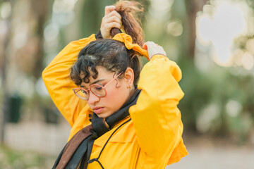 Young woman tying hair while wearing yellow raincoat in park during winter flu season