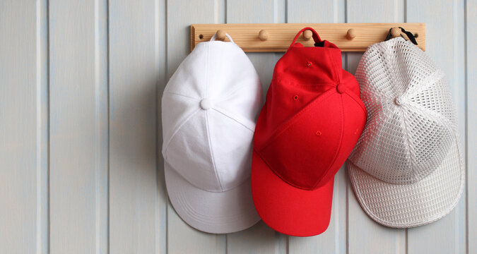 Different baseball caps hanging on wooden wall rack displaying variety and style