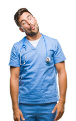 Young handsome doctor surgeon man over isolated background making fish face with lips, crazy and comical gesture. Funny expression.