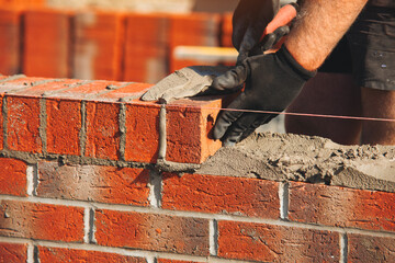 Close-up of Skilled bricklayer constructs a sturdy wall using red bricks and mortar at a...