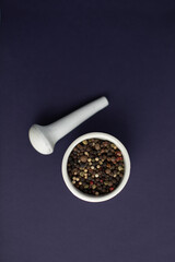 White mortar and pestle with peppercorns on a purple background