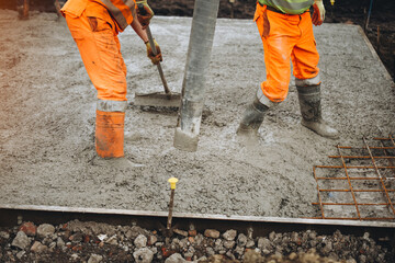 Construction workers pouring concrete for foundation during daylight hours in orange safety gear