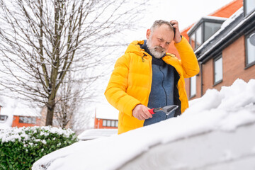 Man clears snow from car with shovel during winter morning in residential area