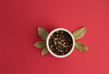 Ceramic mortar and pestle with peppercorns on red background. Black pepper and bay leaf in a white bowl on a red background