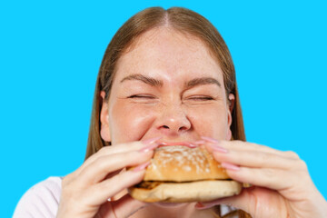 Woman enjoying a delicious burger with a joyful expression against a bright background
