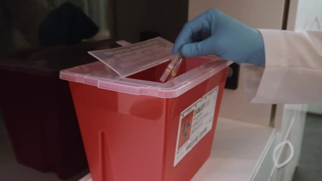 Gloved hand throw used disposable medical waste in sharps container