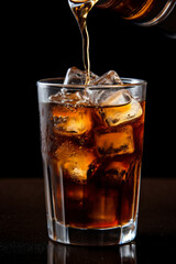 Glass of cola with ice cubes being poured, showing bubbles and caramel color.