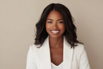 Obraz premium Portrait of a joyful accomplished Black businesswoman in a white jacket smiling against a plain beige background