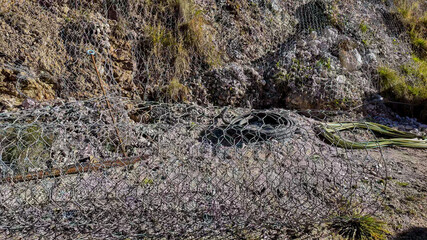 A rocky hillside with erosion control mesh and cables illustrates infrastructure erosion prevention...