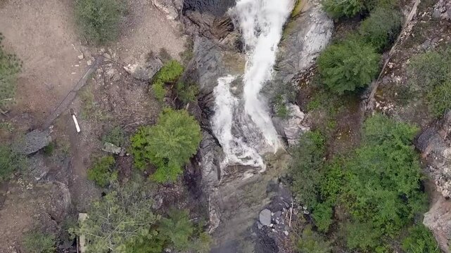 Flyover looks directly down onto waterfall flowing in steep rock canyon