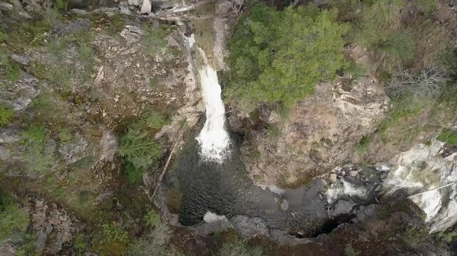 Mountain creek flows over waterfalls in deep rock canyon, aerial