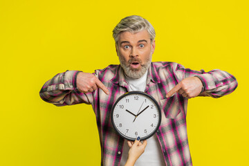 Mature man lifts office clock with worried face highlighting close call and racing anxiety. Guy conveys overwhelming deadline rush signaling imminent lateness deadline, worrying to be punctual, stress