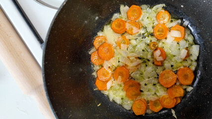 Sliced carrots and onions frying in a black pan, perfect for healthy cooking concepts or vegetarian holiday meals