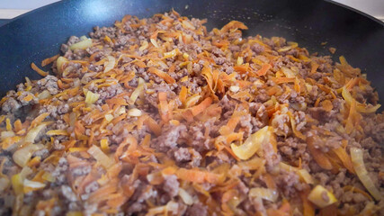 A close-up of minced meat, onions, and carrots sizzling in a pan, ideal for homemade Bolognese sauce recipes