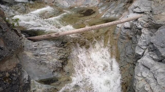Huge log jammed onto rocks at top of rugged canyon waterfall cascade