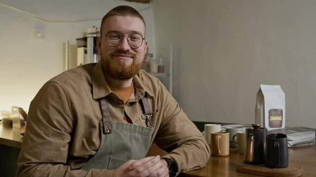 Medium portrait of young male entrepreneur in apron smiling at camera while working at roastery