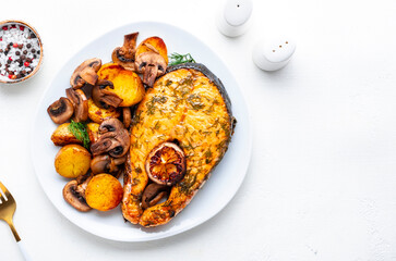 Baked salmon steak with lemon and dill, fried baby potatoes with mushrooms and cream sauce. White background, top view