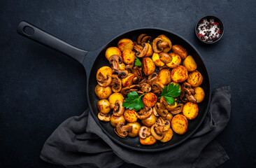 Boiled and fried potatoes in peels with champignon mushrooms and spices in frying pan. Black...