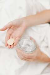 Woman in bed holding glass of water and pill, with bowl next to her