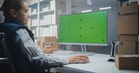Naklejka premium Distribution Center: Female Logistics Specialist Works on Computer in Warehouse Facility, Enters Data, Checks Inventory or Parcels Information. PC Screen Shows Green Screen Chroma Key. Dolly Shot.