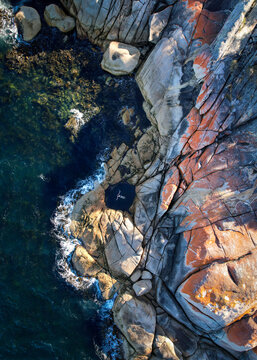 Aerial view of woman swimming in a rock pool near the ocean and rock cliffs 
