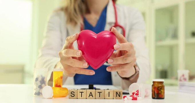 Woman shows heart shaped toy above Statin word from cubes at workplace in clinic. Cardiologist explains medication for cardiovascular health