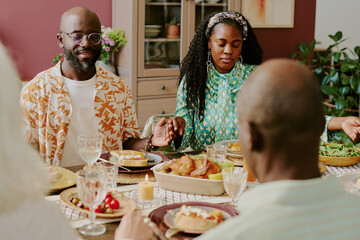 African American married couple sitting at holiday table holding hands while praying together