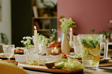 Medium close up of fresh fruits on wooden cutting board and crystal jar of homemade citrus lemonade with kiwi and mint