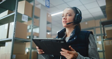 Female Logistics Coordinator, Manager Wearing Headset Chats to Customer, Uses Tablet Computer in...
