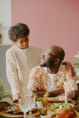 Vertical shot of African American boy hugging his father who sitting at festive table while they looking at each other