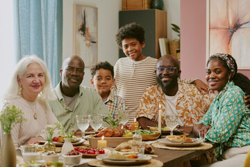 Medium close up portrait of biracial family sitting at festive table with huge number of treats smiling at looking at camera