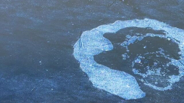 Stone flies onto frozen surface of river, breaks ice and creates splashes.