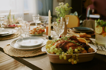 Medium close up of roasted chicken with golden crust surrounded with grapes and juicy slices of orange on served table