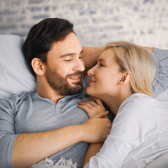 Portrait image - young adult couple sleeping, lying in bed, against bricks wall background. Blond woman with brunette hair man in love, relationship, dates, happy family, wait child concept. Square
