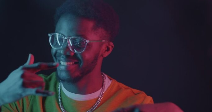African American man dancing having fun in neon light on dark background. Youth culture and modern entertainment concept.