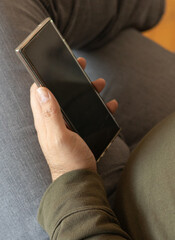 Man in casual clothes holding smartphone, checking messages while sitting.
