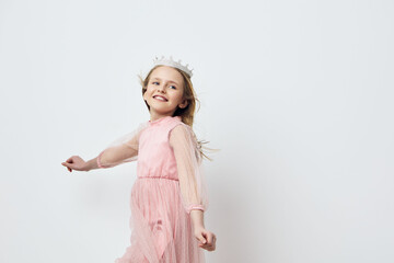 Cheerful girl in a pink dress with a crown, joyfully twirling against a white background, embodying childhood happiness and innocence