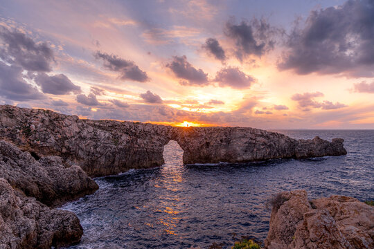In the middle of the Mediterranean we see the beautiful natural rock arch, Pont d en Gil in Menorca Spain. The combination of sea, rocks and sky creates a great atmosphere, near Ciutadella, Menorca