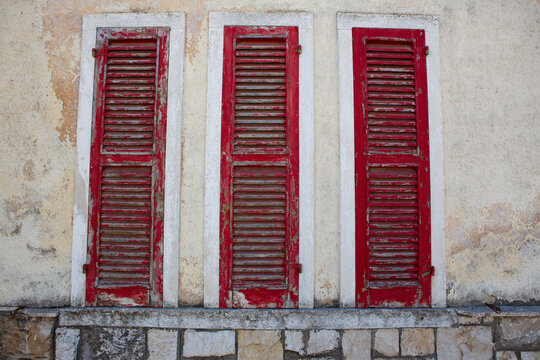 Old damaged red shutters on a rustic mountain village house window in Italy. Unique architectural detail reflecting Italian countryside charm. - Powered by Adobe