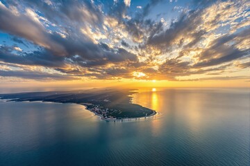 Obraz premium A stunning aerial view of a coastline during sunset, featuring dramatic clouds and golden light over a serene blue sea. Natural beauty and tranquility concept. Ai generative