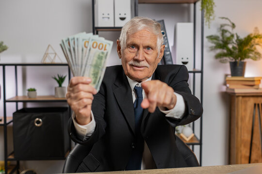 Rich old grandfather businessman freelancer working at home office workplace counting money dollar cash, calculate earnings income profit pointing at camera. Business people. Employment occupation