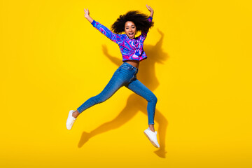 Full length photo of lovely young lady excited jump raise hands dressed stylish colorful blue garment isolated on yellow color background